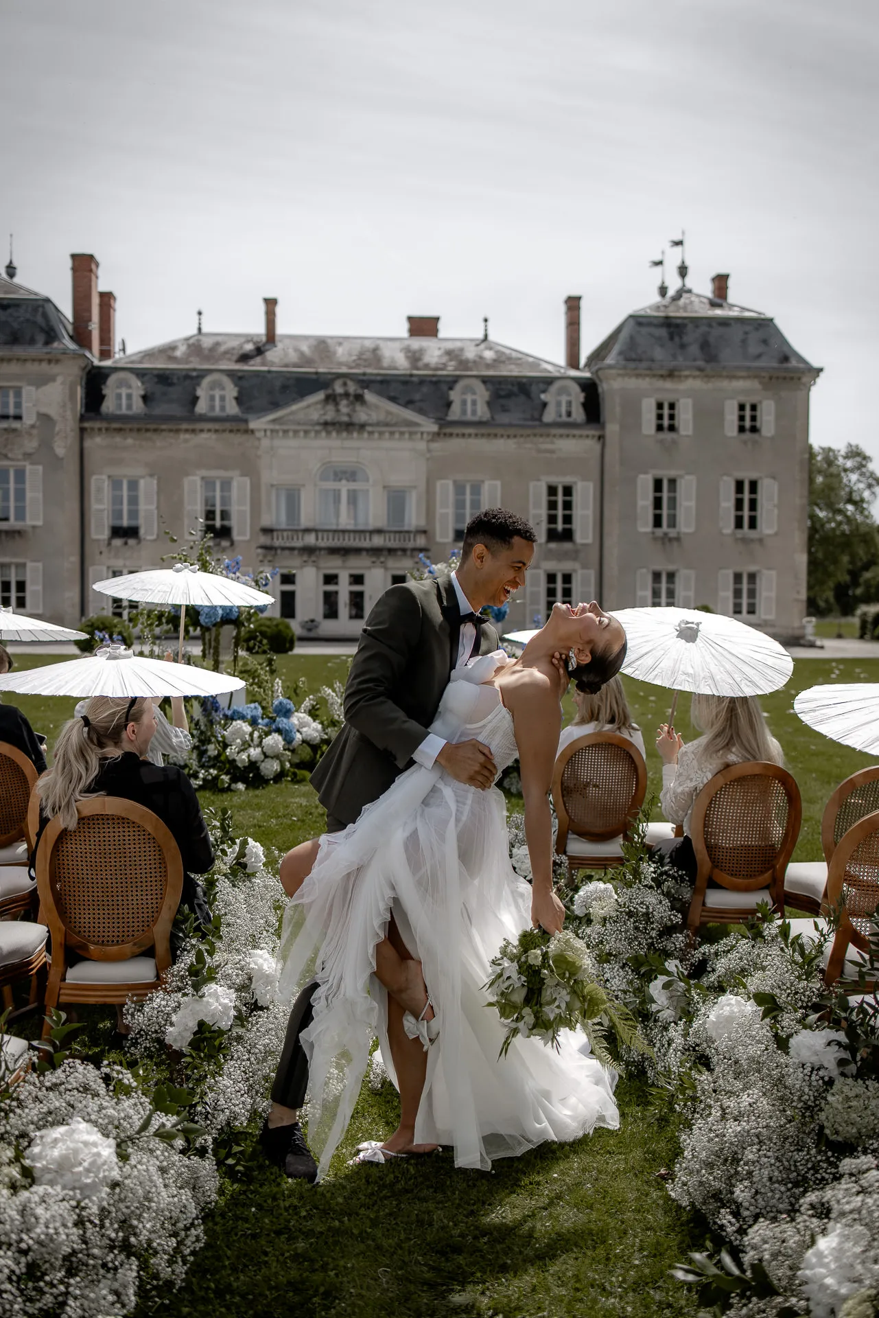 Romantic kiss of bridal couple after ceremony at Chateau de Varennes with white parasols